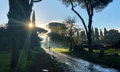 A man jogs on the ancient Appian Way in Rome as dawn breaks behind mature trees that line the pathway