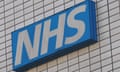 A white-on-blue sign that says NHS on the outside of a building that is all dingy, rectangular white tiles.