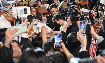 Timothée Chalamet surrounded by fans taking pictures.