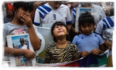 A young girl sobs among a crowd of mourners, some holding memorial photographs