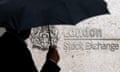 A man shelters under an umbrella as he walks past the London Stock Exchange