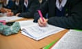 A student writes with a pink pen in an exercise book at a school desk in a classroom