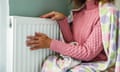 A woman in a warm jumper and covered with a blanket trying to keep warm by a radiator.