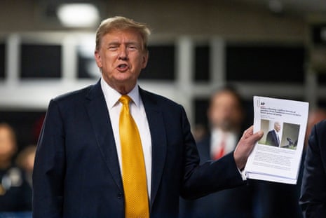 a man in a dark suit and yellow tie holds up a stack of papers