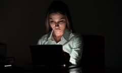 Young woman sitting at desk and using a laptop in the dark