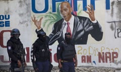 Police stands before a mural of Haiti’s President Jovenel Moïse, who was assassinated last week, days after another 15 Haitians were gunned down.