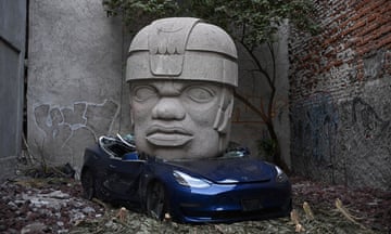 An artwork by Chavis Mármol of a Tesla 3 car being crushed by a nine-tonne Olmec-inspired head