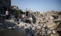 Palestinians examine buildings and collect remaining belongings from heavily damaged houses after Israeli attacks on Maghazi refugee camp: a man stands on the edge of a pile of rubble in a scene of devastation in which mattresses, bedding and other household items are seen.