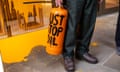 A person stands in front of a window covered in orange pain holding an orange cylinder with the words 'Just Stop Oil' on it