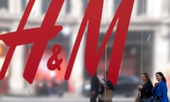 People passing a large sign for the clothing brand H&M