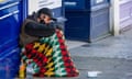 Homeless man sitting on a pavement wrapped in a colourful blanket