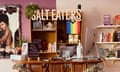 A colorful image of a rattan checkout table with two computers, hand sanitizer and a stack of books, decorated with gold tinsel, beyond which is a bookshelf with a Pride flag, letters spelling out Salt Eaters Bookshop, and images of Black people.