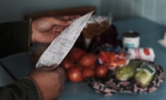 A pair of maybe dirty white hands holds a long white receipt, with groceries blurred on a table in the background.
