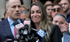 A woman and a man speak into a clump of mics in front of them. A crowd stands behind them