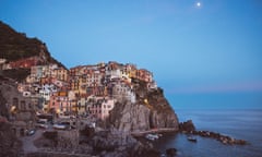 A clutch of buildings on a hillside, perched near rugged rocks by the sea