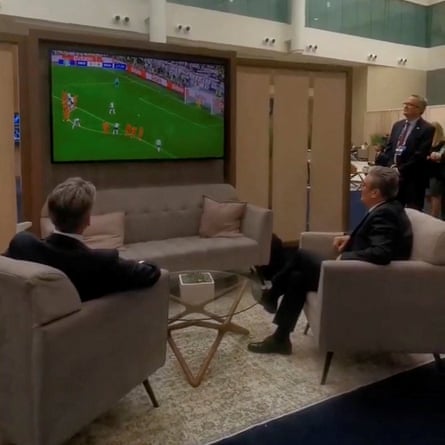 Keir Starmer watching football on a screen with another man with his back to the camera