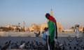 Man wearing Palestinian flag feeds birds near Fanar Mosque