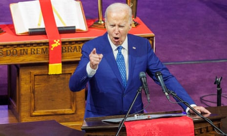 white man wearing blue suit and blue tie gestures and speaks in front of microphones