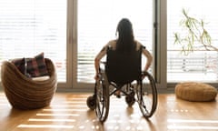 A young disabled woman in a wheelchair at home, seen from behind