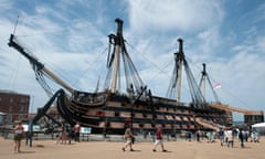 HMS Victory in Portsmouth, against a slightly cloudy sky, with tourists in shorts walking towards the gangplank