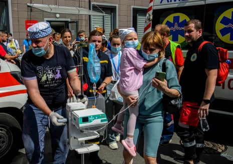 Medics carry a little girl and equipment at the site of a missile strike