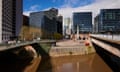 A low and brown-looking river flowing underneath two bridges, with office buildings or blocks of flats in the background