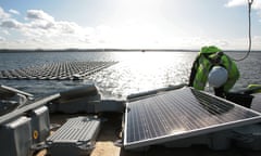 A worker in hi-vis jacket at work on a floating solar panel array on London’s Queen Elizabeth II reservoir