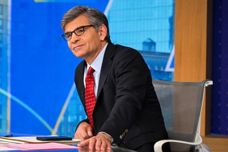 a man in a suit and tie sits at a desk on the set o fa show