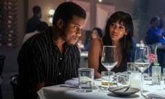Black man sitting at table looks down as Black woman looks at him
