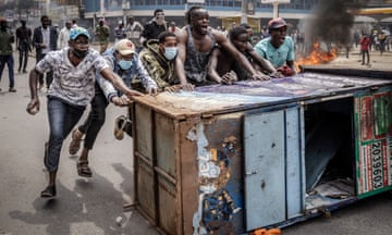 Angry-looking people behind old cupboard used as barricade with smoke and fire in background