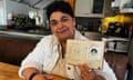 A middle-aged woman sits in a tidy kitchen and show off her passport from when she was an infant.