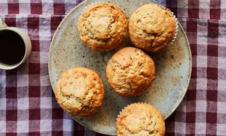 Aerial image of five banana muffins on a rustic plate next to a cup of black coffee. The items are on a burgundy gingham tablecloth 