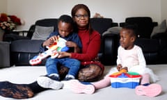 Perpetual Uke sitting on a white carpet in front of a black leather sofa and chair, with a little boy, Pascal, sitting on her lap holding a toy guitar, and his twin sister, Palmer, sitting next to her playing with another toy