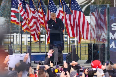 a man speaks in front of American flags