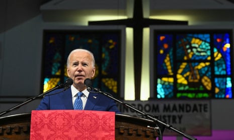 white man wearing blue suit and tie stands in front of two microphones with a big cross behind him