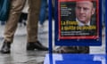 A poster of French President Macron on a news stand in the rain as people walk by