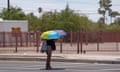 A person shields themselves from the sun with a rainbow umbrella.