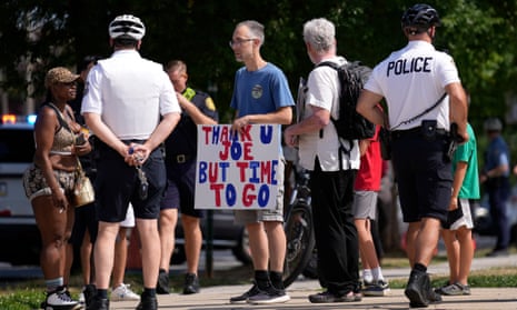 people stand around white man wearing blue shirt holding red, white and blue sign