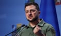 Volodymyr Zelenskiy speaking in front of a blue backdrop