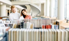 Two smart students reading and studying in library whole searching through books on the shelves<br>G1959C Two smart students reading and studying in library whole searching through books on the shelves