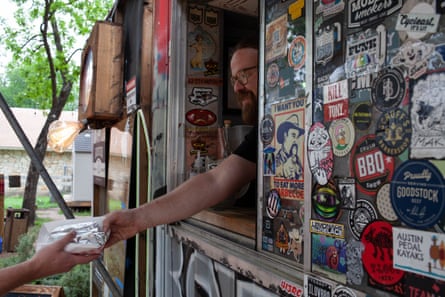 A bearded man hands a wrapped meal to a customer from a food truck.