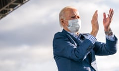 Joe Biden, wearing a mask, claps on stage