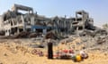 A woman stands with salvaged items near a damaged building