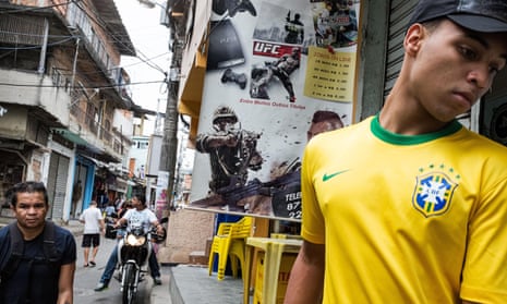 A resident stands in front of an advertisement for online combat games on the streets of Complexo do Alemao, Brazil