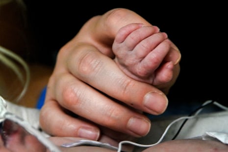 an adult hand holds the hand of a premature baby