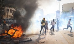 Young men with their faces covered running down a street as black smoke billows from a bonfire