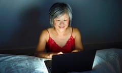 A mature woman in a red negligee flirts online in bed.