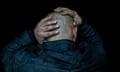 Closeup of back of a man's shaven head as he clutches it with his hands, in a gesture of despair.