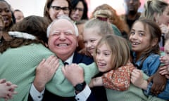 A gray-haired, balding man grins as children hug him.