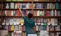 Rear view of man removing book from shelf while standing in store.